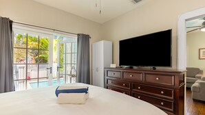 Una habitación de hotel con una cama grande, televisión, cómoda y vista a una piscina.