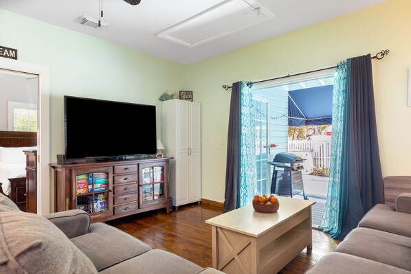 A living room with a flat-screen TV, a cabinet with games, a sofa, and a table with oranges.