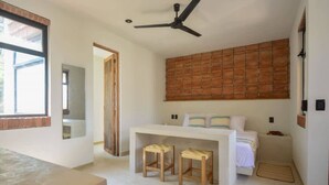 Een slaapkamer met een bed, een bureau, twee krukken, een plafondventilator en een raam.