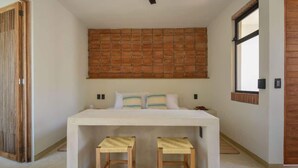 Een slaapkamer met een bed, twee krukken, een metselwerk muur, een raam en een deur.