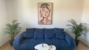 Una sala moderna con un sofá azul, dos mesitas y dos plantas en macetas.