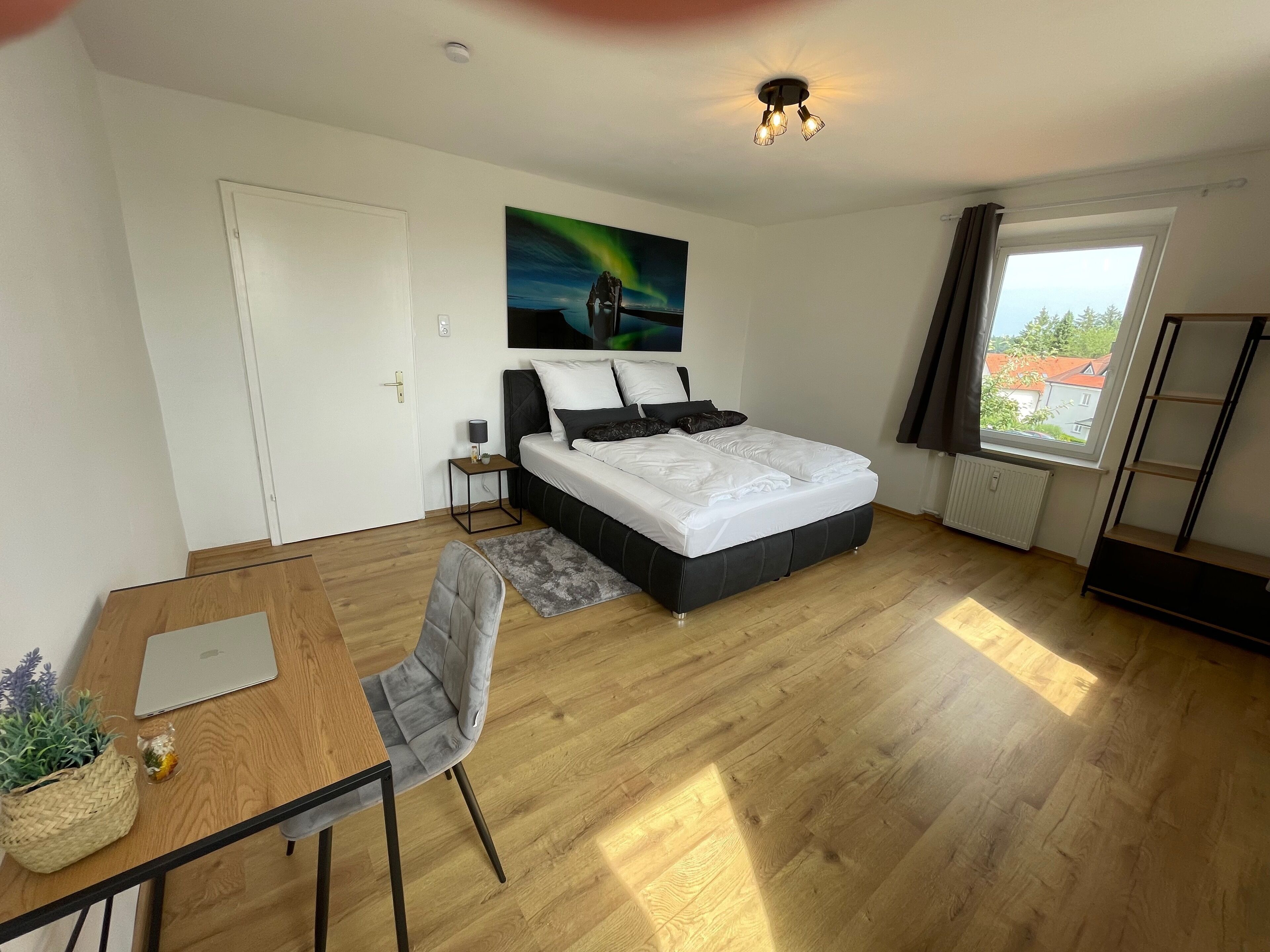 Een moderne slaapkamer met een bed, een bureau, een stoel, een raam met uitzicht en een plafondlamp.