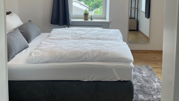 Un dormitorio con una cama grande, una ventana con vistas a la vegetación, un lámpara en el techo y un espejo en la pared.