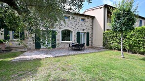 Un edificio de piedra con un patio de piedra, asientos al aire libre y un jardín césped.