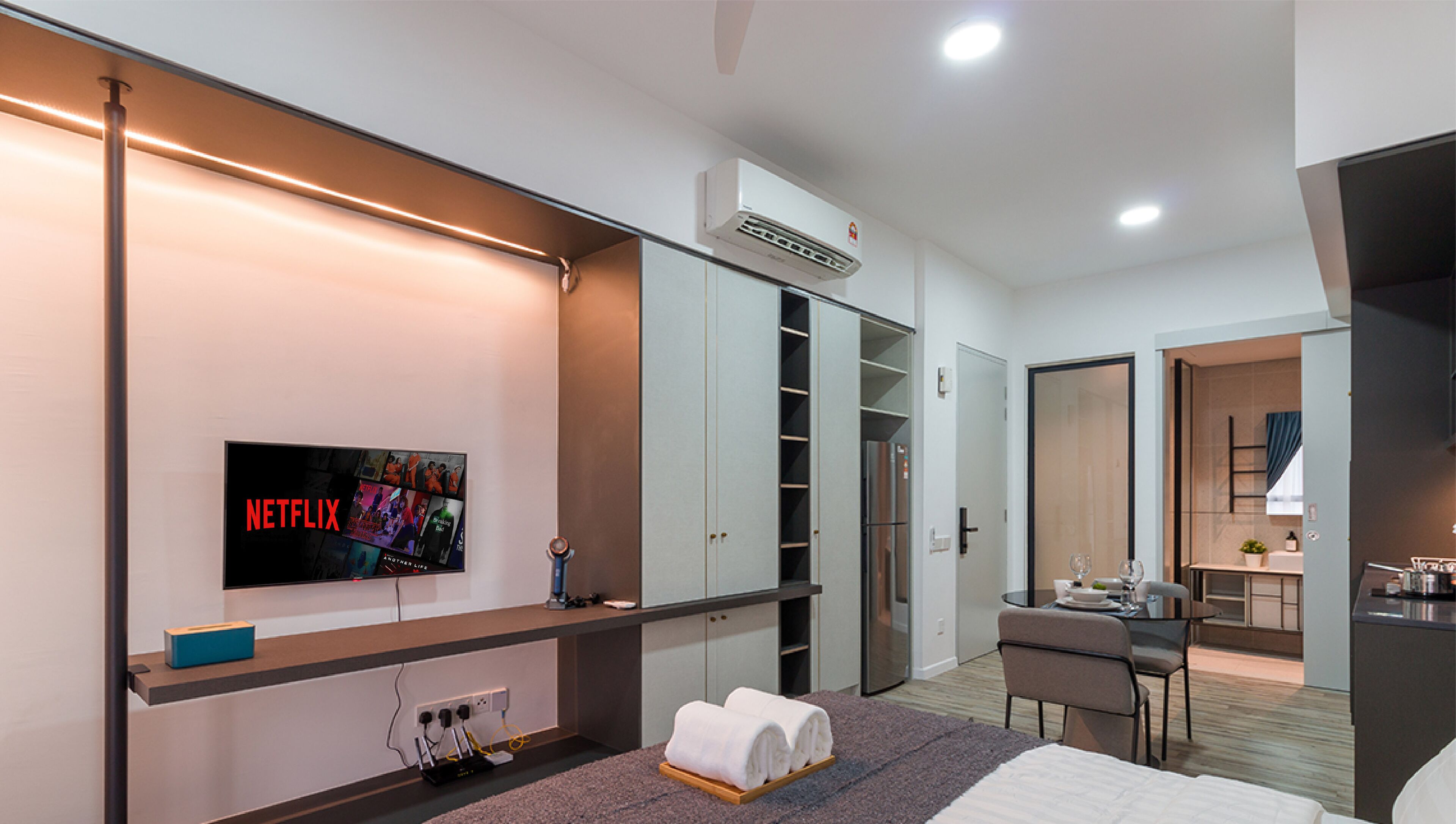 Une chambre d’hôtel moderne équipée d’une télévision à écran plat avec accès à Netflix, d’un minibar, d’un bureau avec une chaise, d’une kitchenette et d’un dressing.