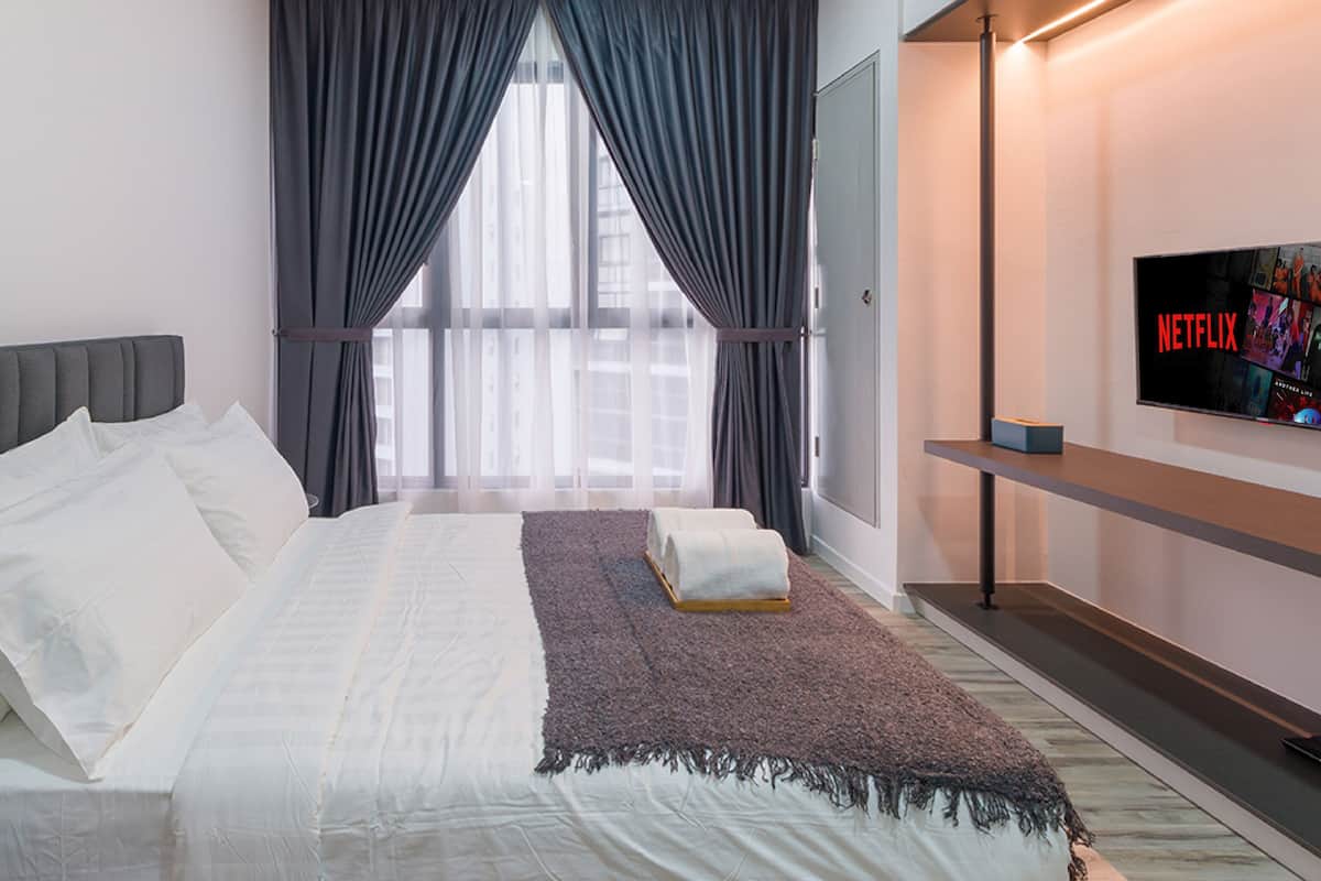A modern hotel room with a large bed, a TV mounted on the wall, and a window with curtains.