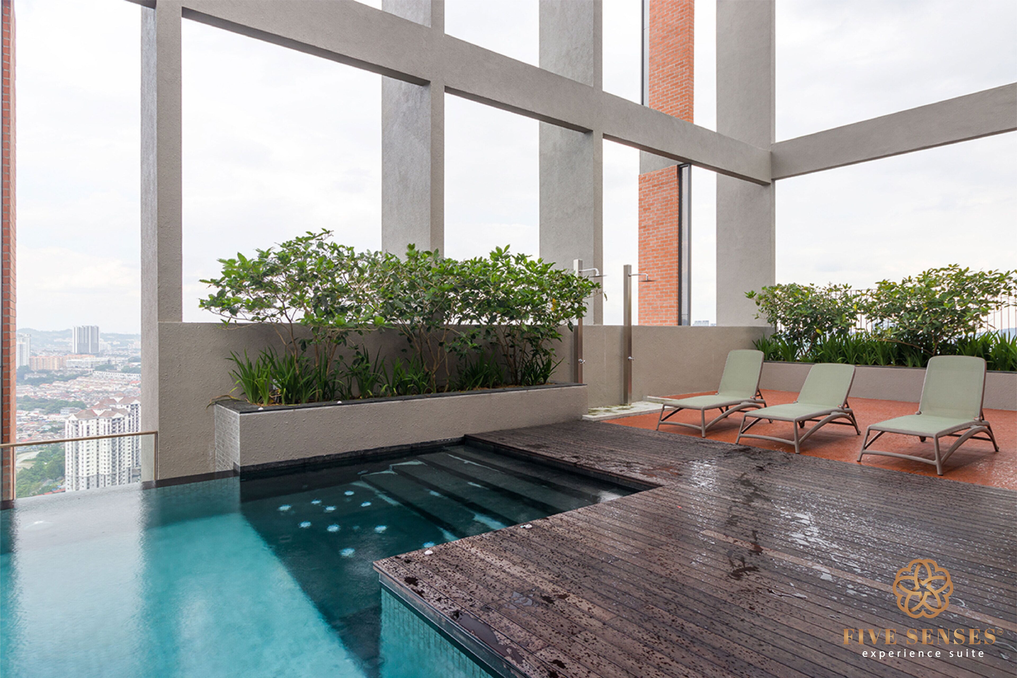 A rooftop infinity pool with a wooden deck, lounge chairs, and potted plants.