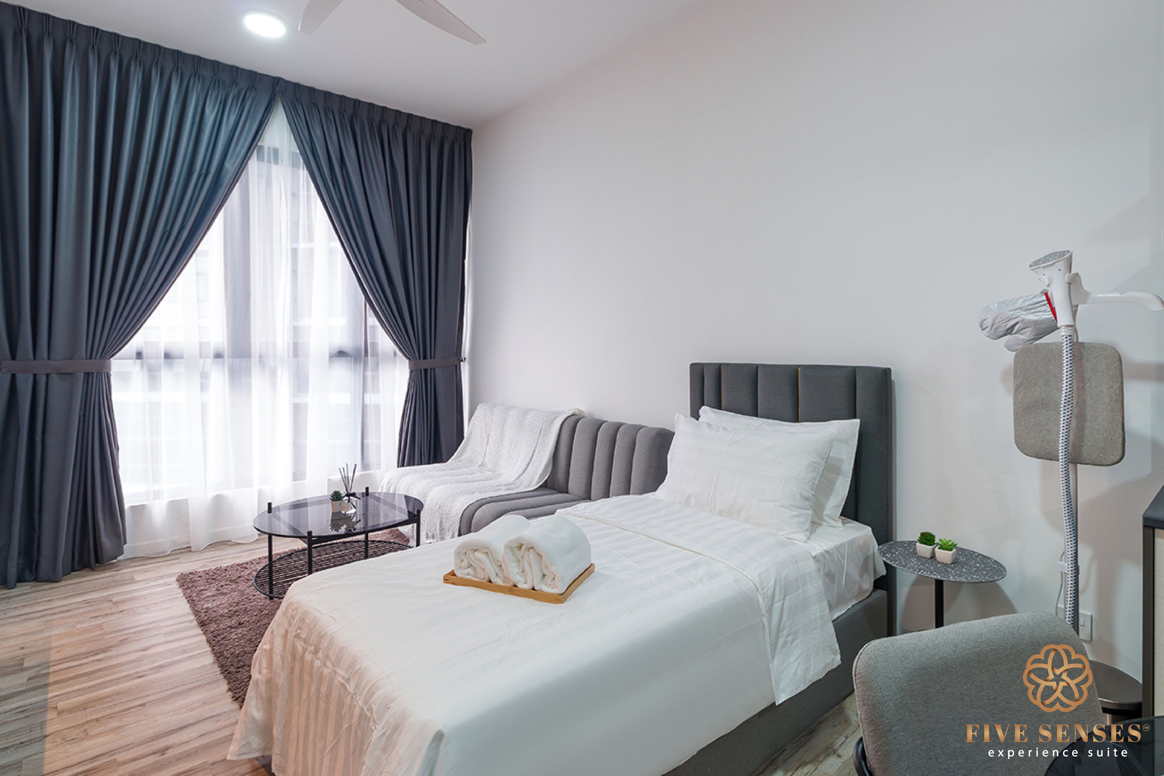 A hotel room with a bed, a chair, a small table, and a massage chair.