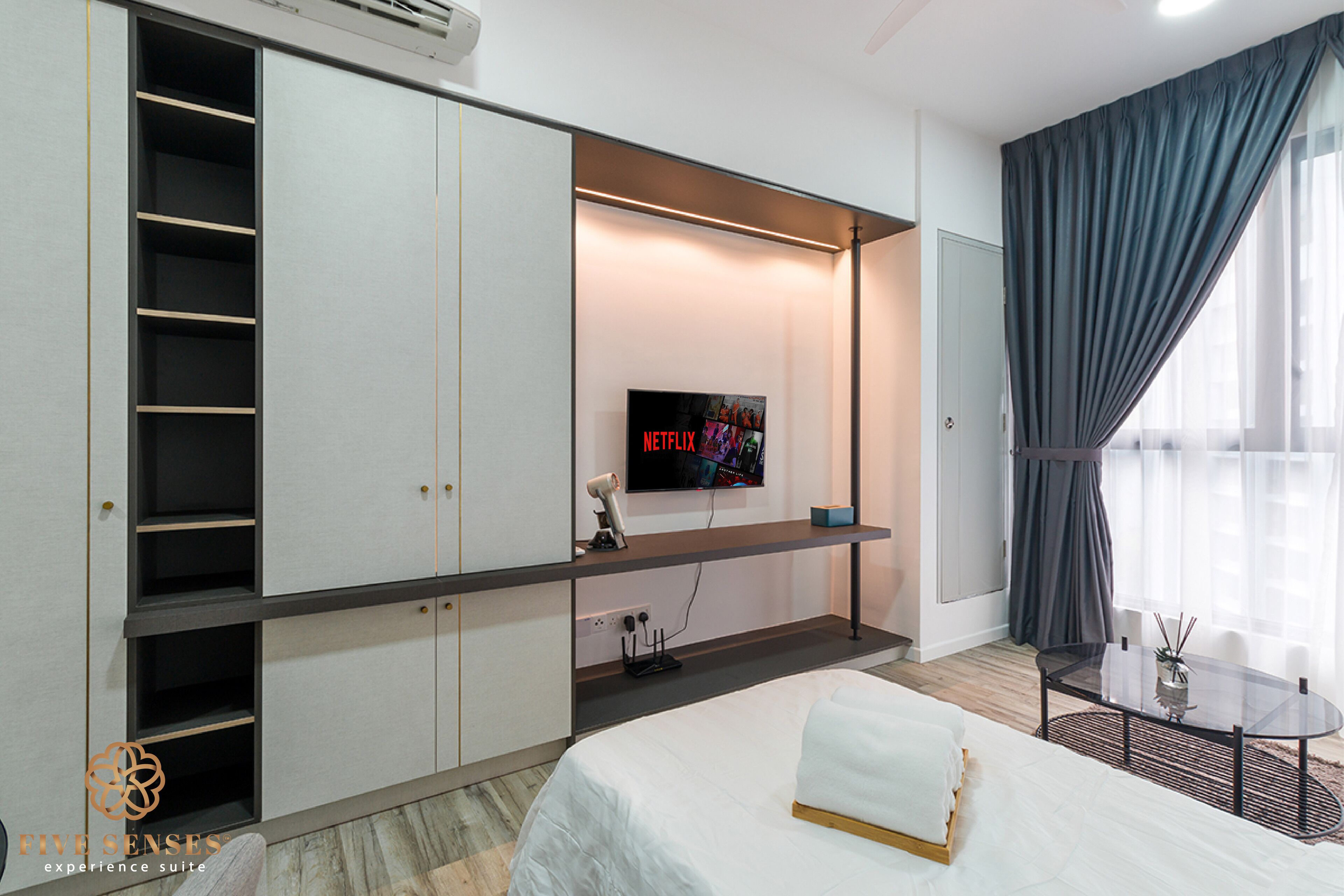 Una habitación de hotel moderna con una cama, un televisor montado en la pared, un escritorio y un amplio ventanal con cortinas.