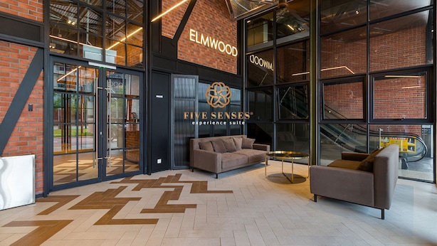 A modern interior with a glass facade, a brick wall, and a logo for 'ELMWOOD'.