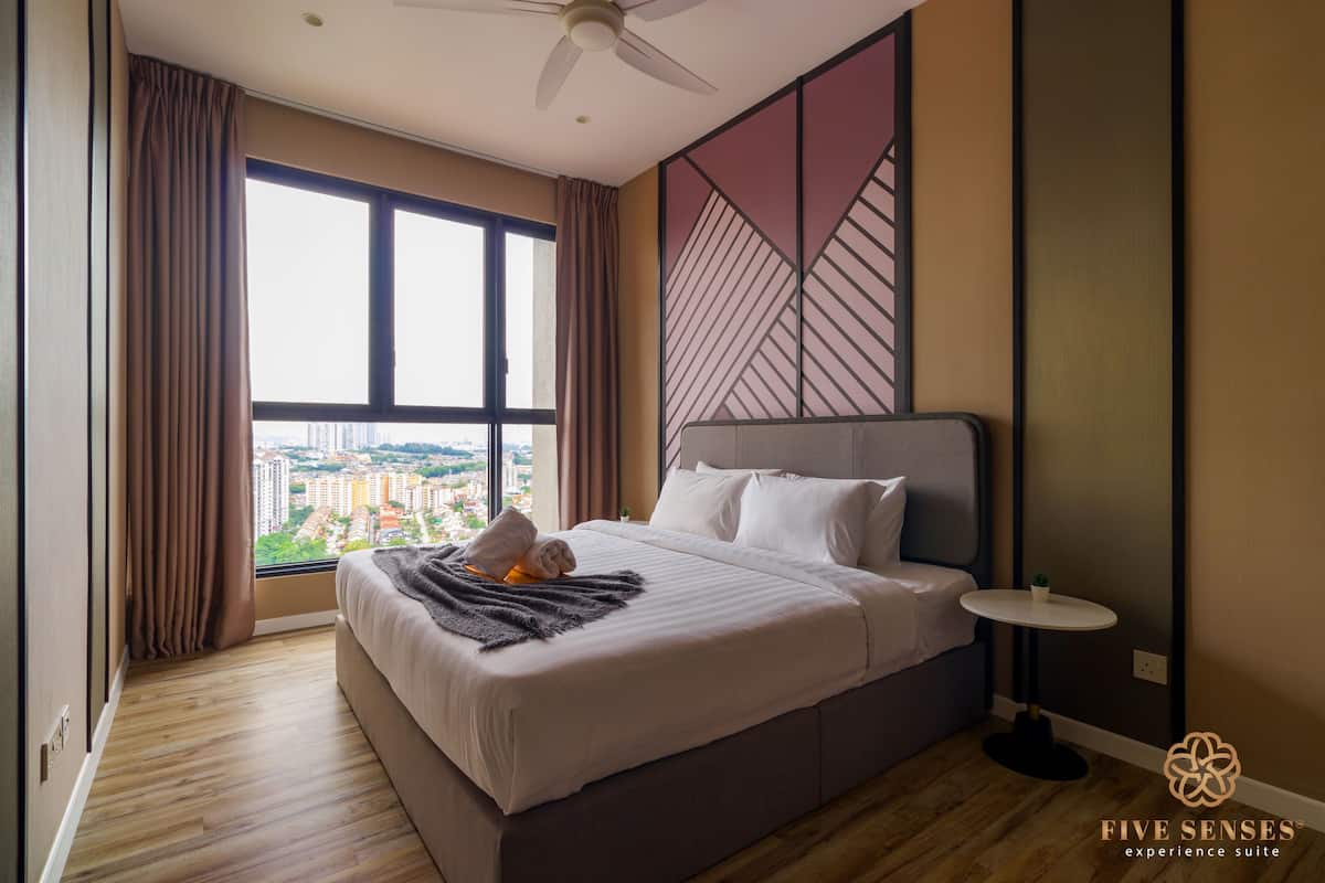 A modern hotel room with a large bed, a small bedside table, and a view of the city through a large window.