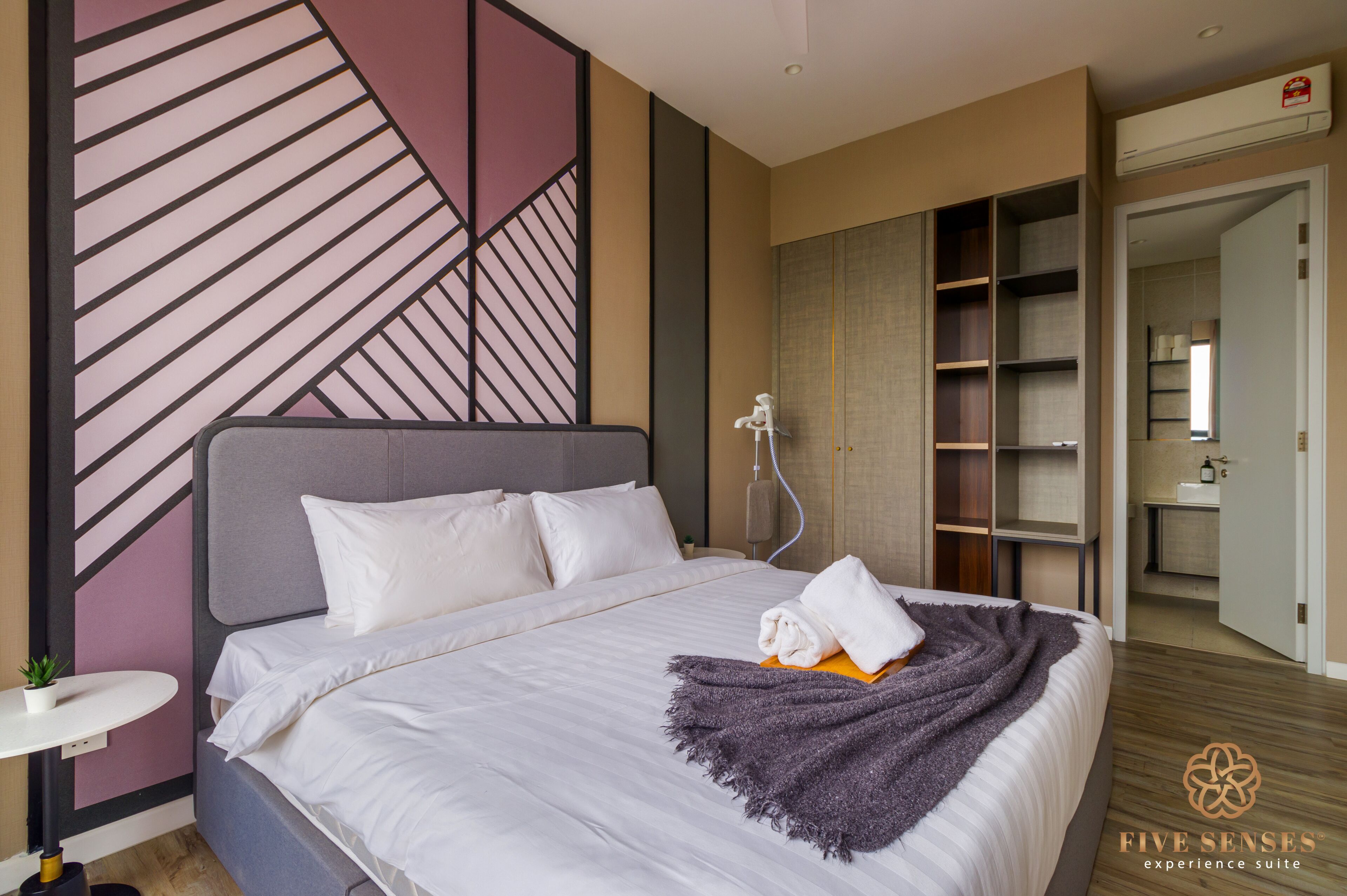 Een moderne hotelkamer met een groot bed, een nachtkastje met een lamp, een kledingkast en een zichtbare badkamer door een geopende deur.