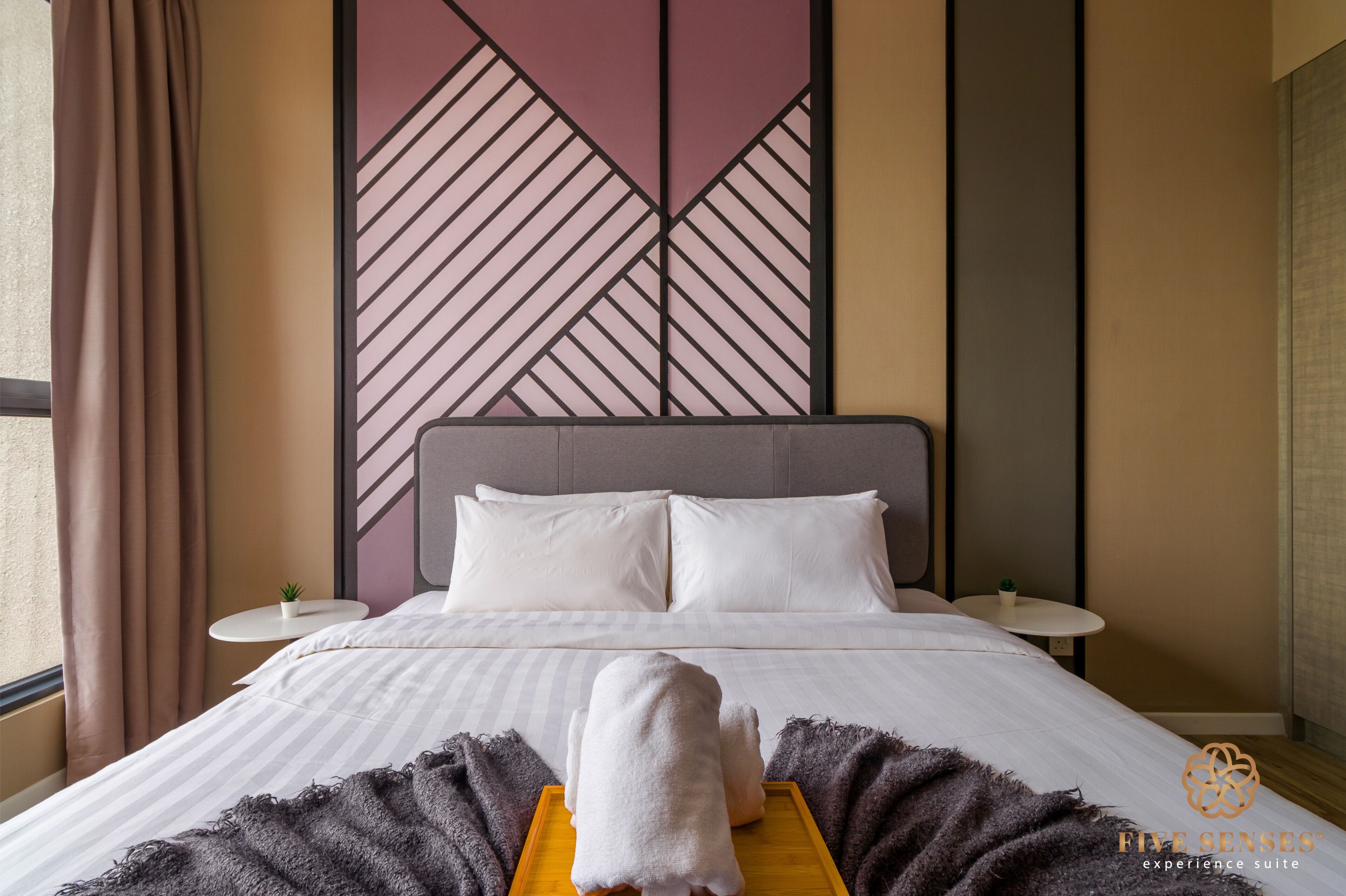 A hotel room with a bed, pillows, a bedside table, a small plant, and a decorative wall panel.
