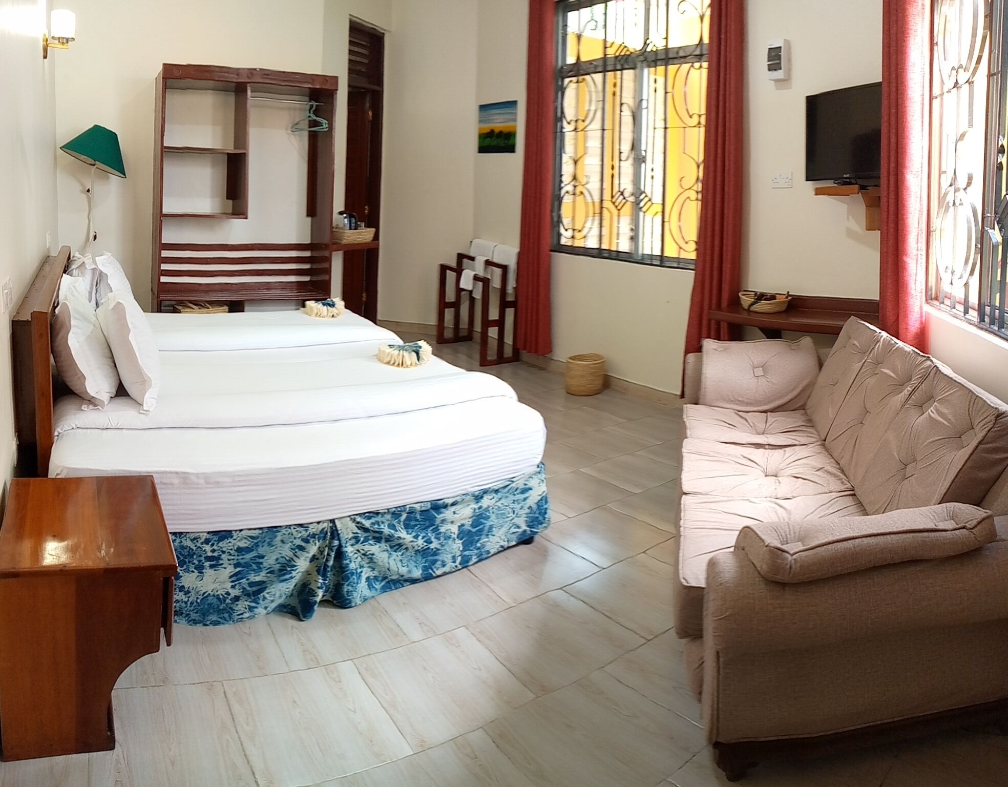 Una habitación de hotel con cama, sofá, televisión y ventana con cortinas.