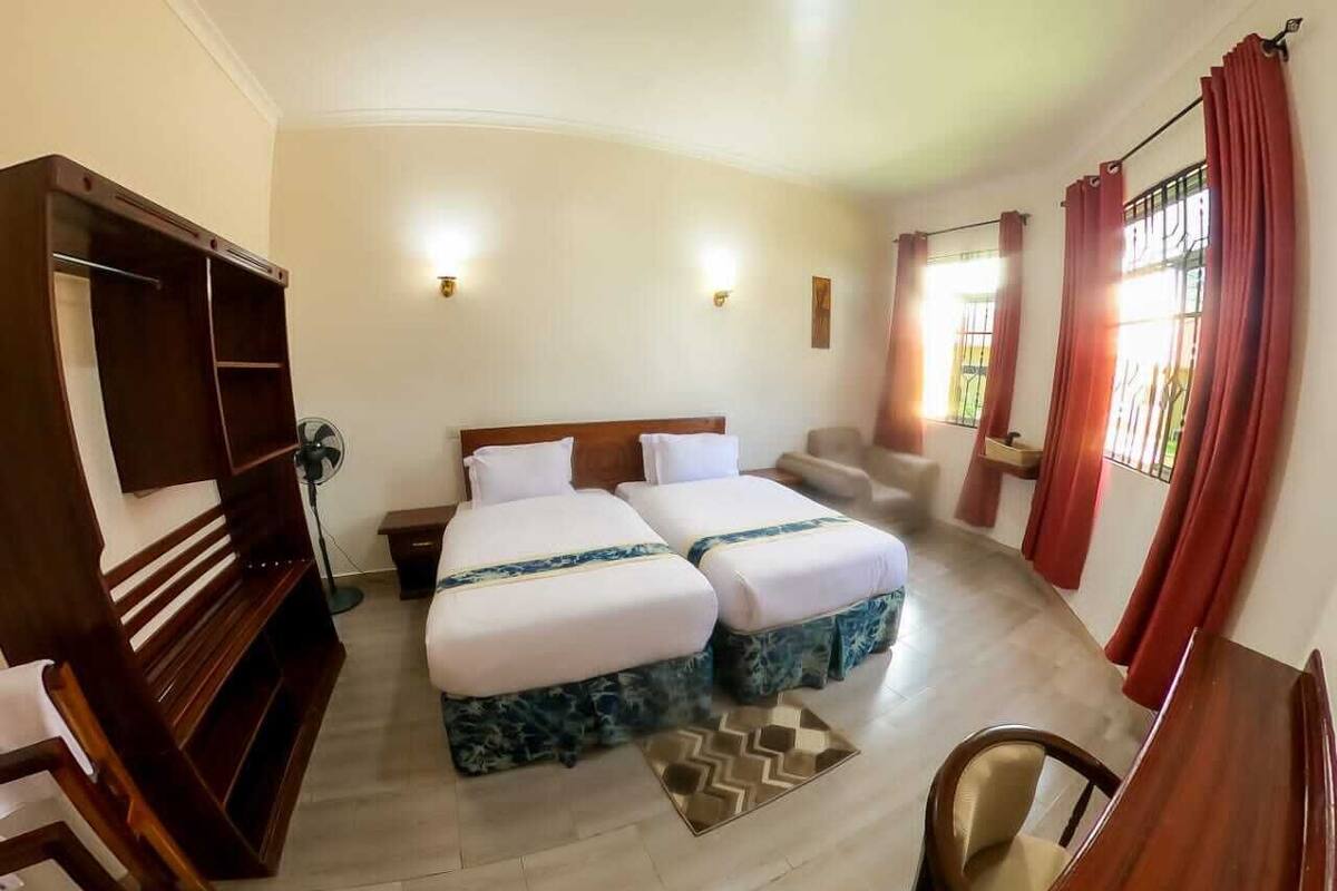 A hotel room with two beds, a wooden bench, a desk, and a chair.