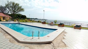 A rectangular swimming pool with two metal ladders, surrounded by a tiled deck with a decorative pattern. - SANDMARK HOTEL SERENGETI  (Bariadi)