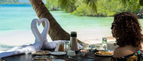 A dining table set for two with plates of food, a coffee pot, and a heart-shaped napkin.
