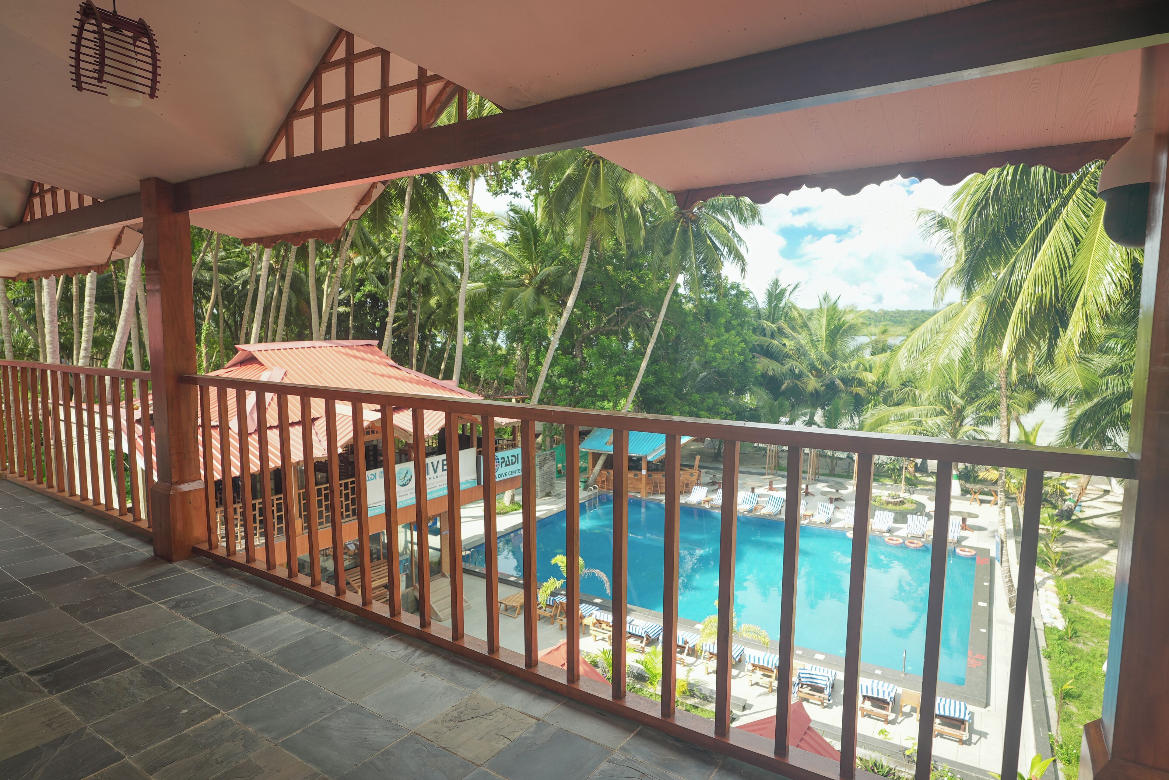 A balcony with a view of a swimming pool, palm trees, and a building with a sign.