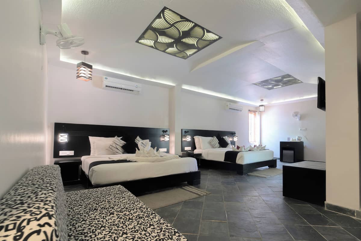 Quarto de hotel moderno com duas camas, um sofá, televisão de tela plana e ventilador de teto.