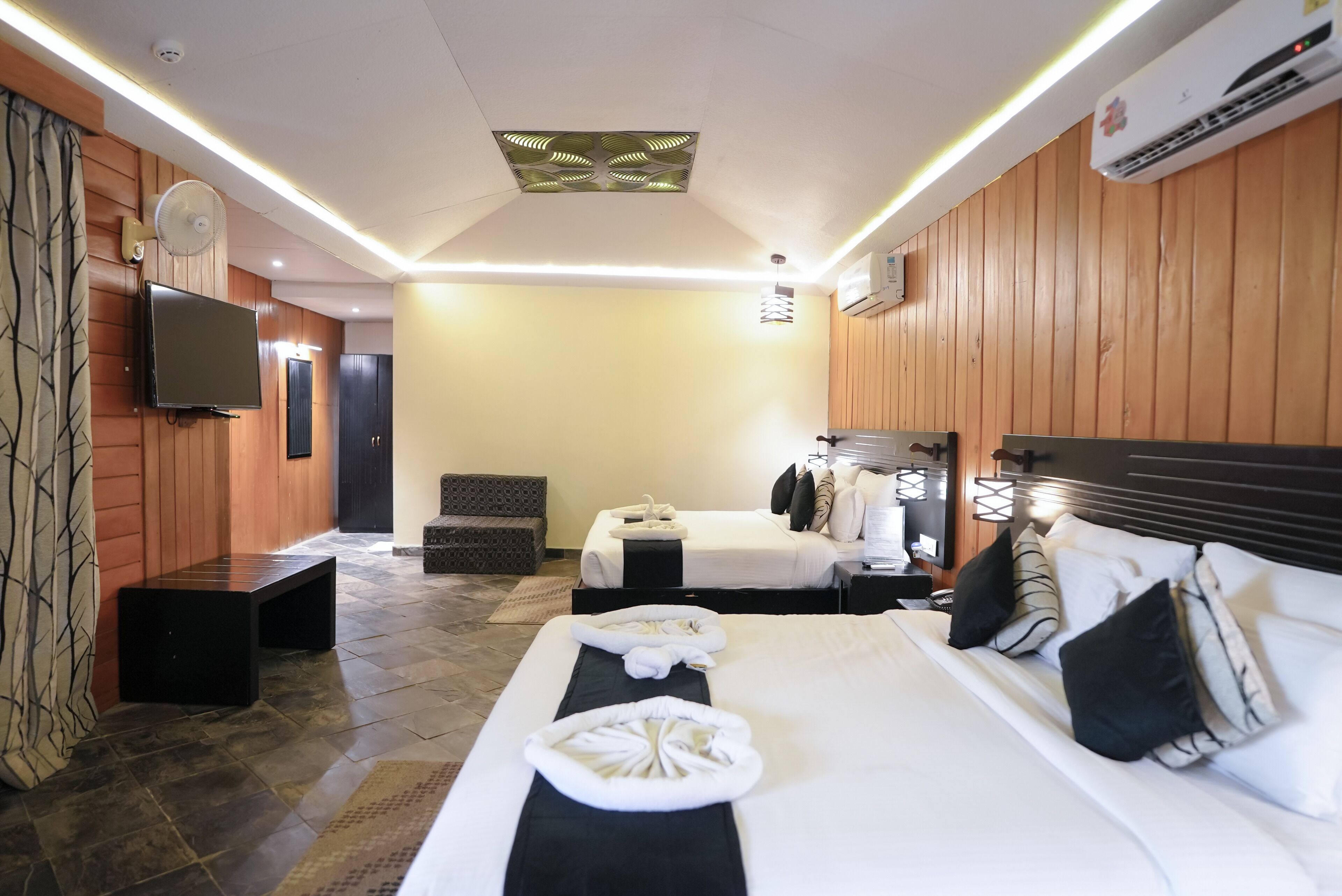 Una habitación de hotel con una cama grande, una cama más pequeña, un televisor de pantalla plana, un ventilador de techo y un equipo de aire acondicionado.
