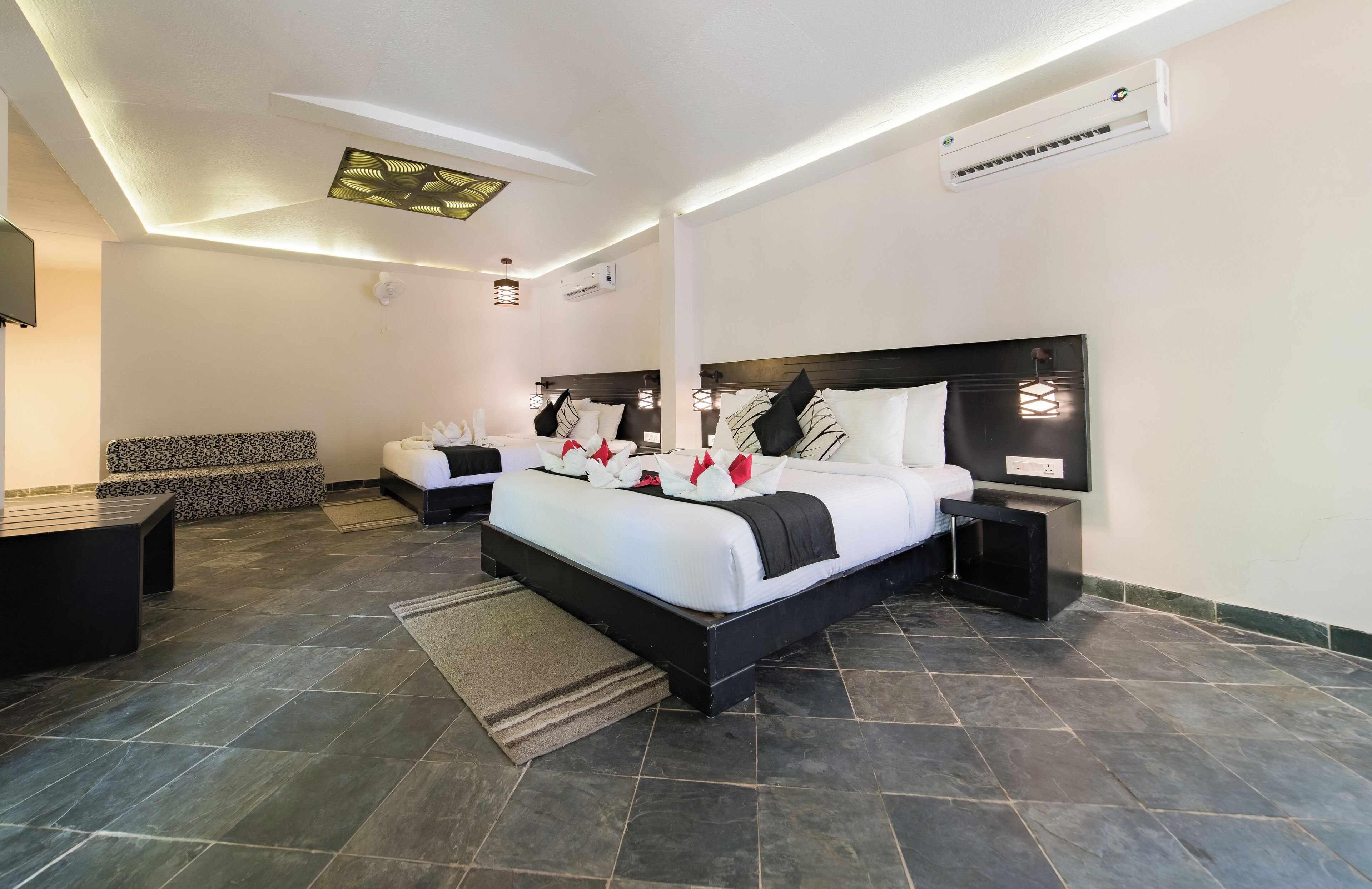 A modern hotel room with two beds, a seating area, and a flat-screen TV.