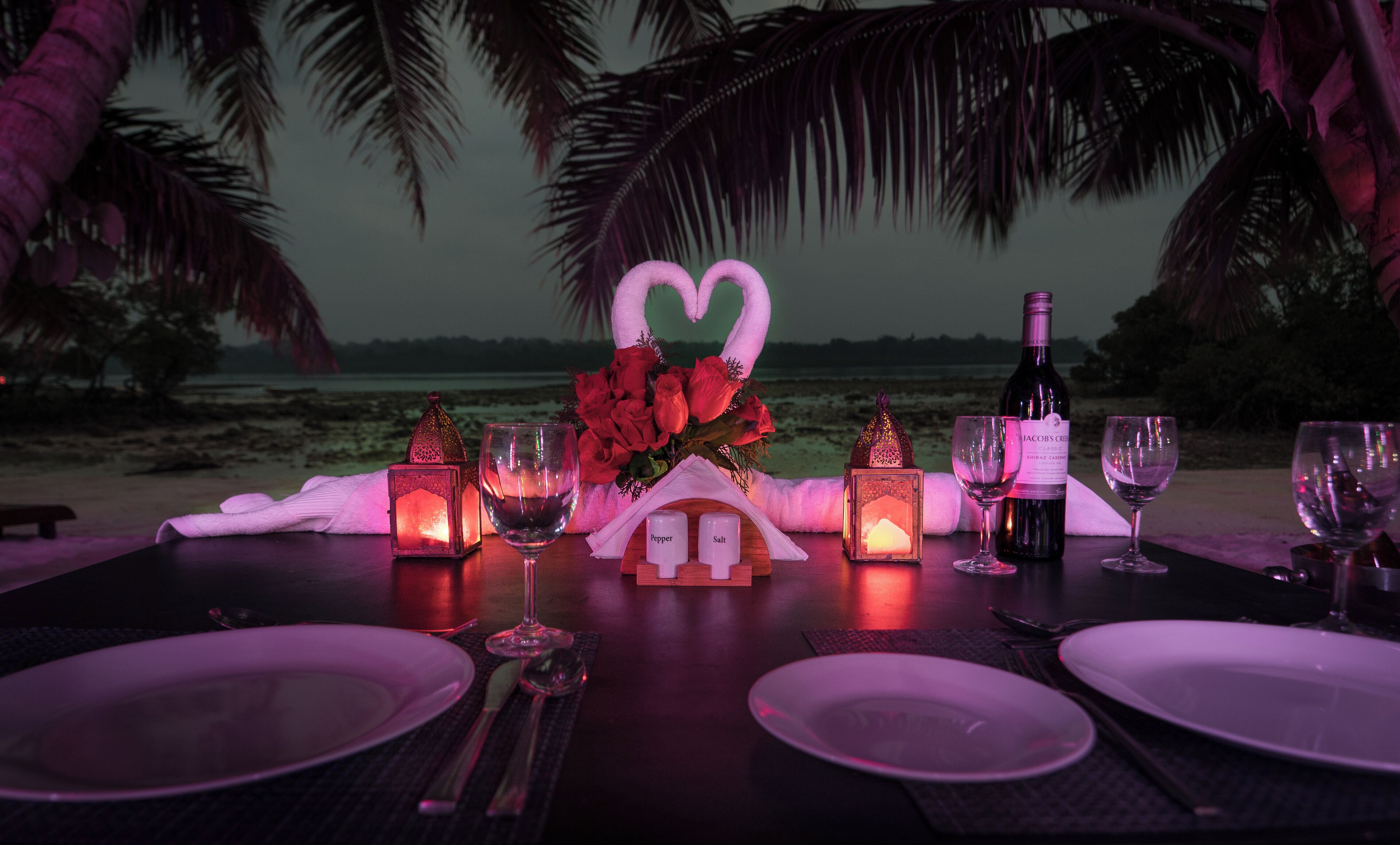 A table set for two with a bottle of wine, glasses, and a centerpiece of red roses.