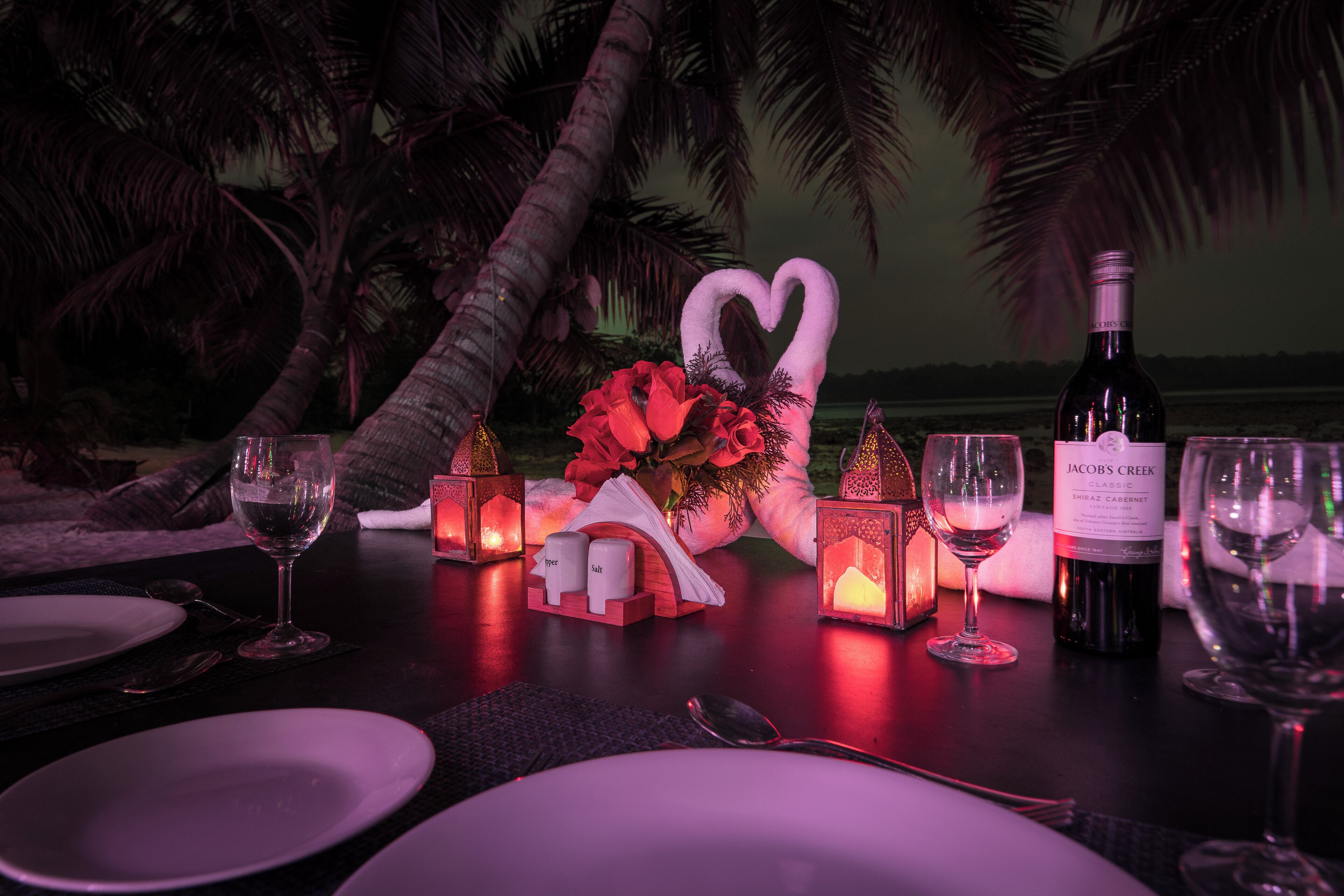 A table set for a romantic dinner with wine glasses, a bottle of Jacob's Creek Classic Shiraz Cabernet, and decorative lanterns.