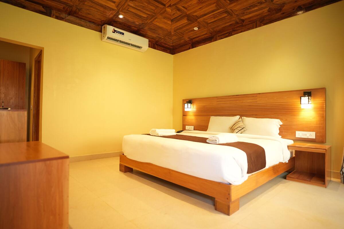 Quarto de hotel com cama de madeira, mesa de cabeceira e teto de madeira.