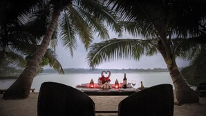 Mesa para dos frente al mar, con una decoración en forma de corazón sobre la mesa, palmeras enmarcando la vista y un cuerpo de agua tranquilo.