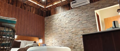 Une chambre spacieuse avec un plafond en bois, un mur en pierre, un lit, une chaise et un bureau avec une lampe.