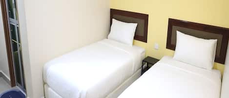 Habitación de hotel con dos camas individuales, una mesita de noche pequeña, aire acondicionado de pared y un cuadro de una cascada.