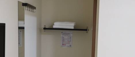 A narrow hallway with a black shelf, a blue pet bowl, and a white wall with a mirror and a notice.