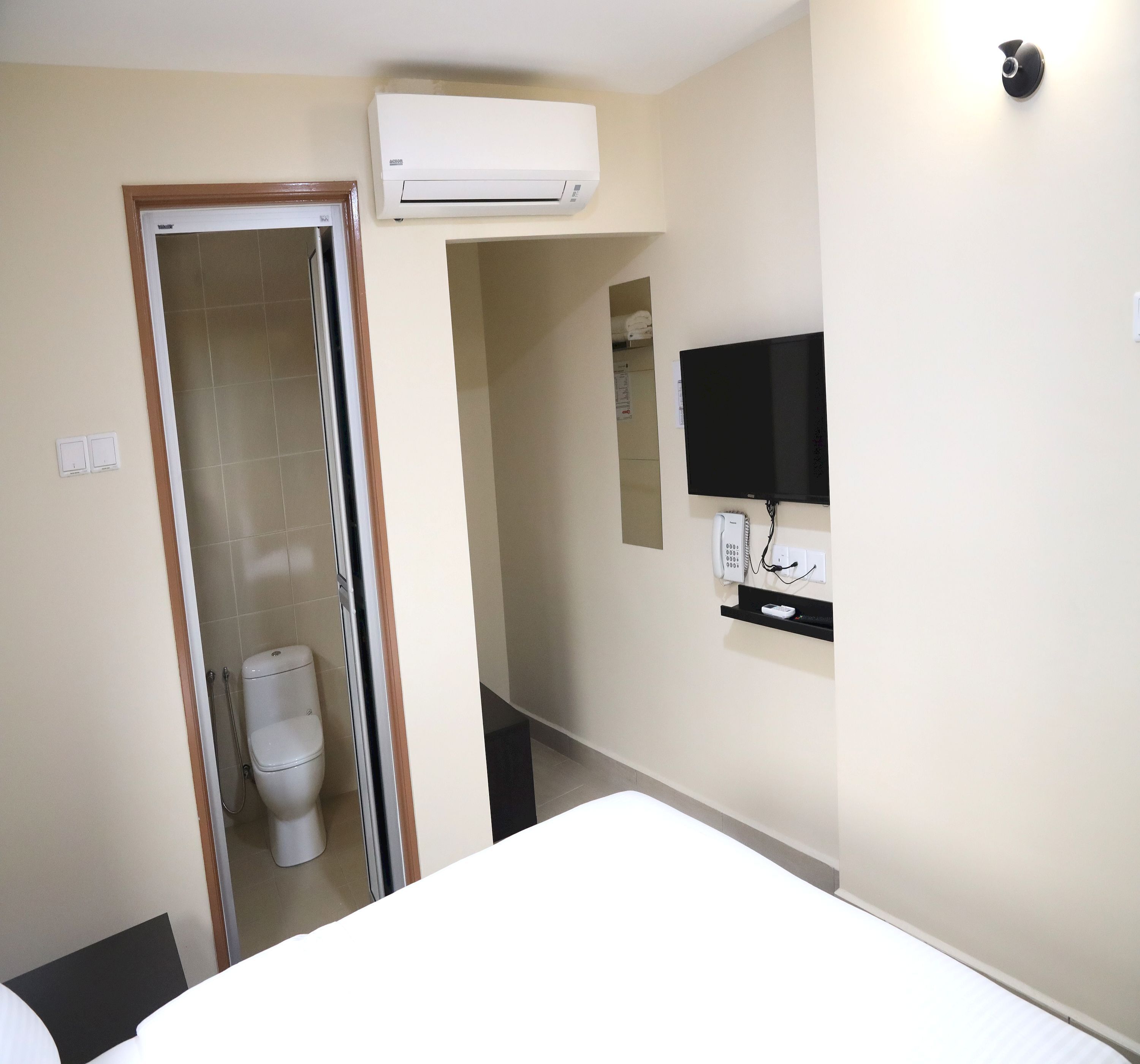 Et hotelværelse med seng, aircondition, toilet, brusebad og et ophængt tv.