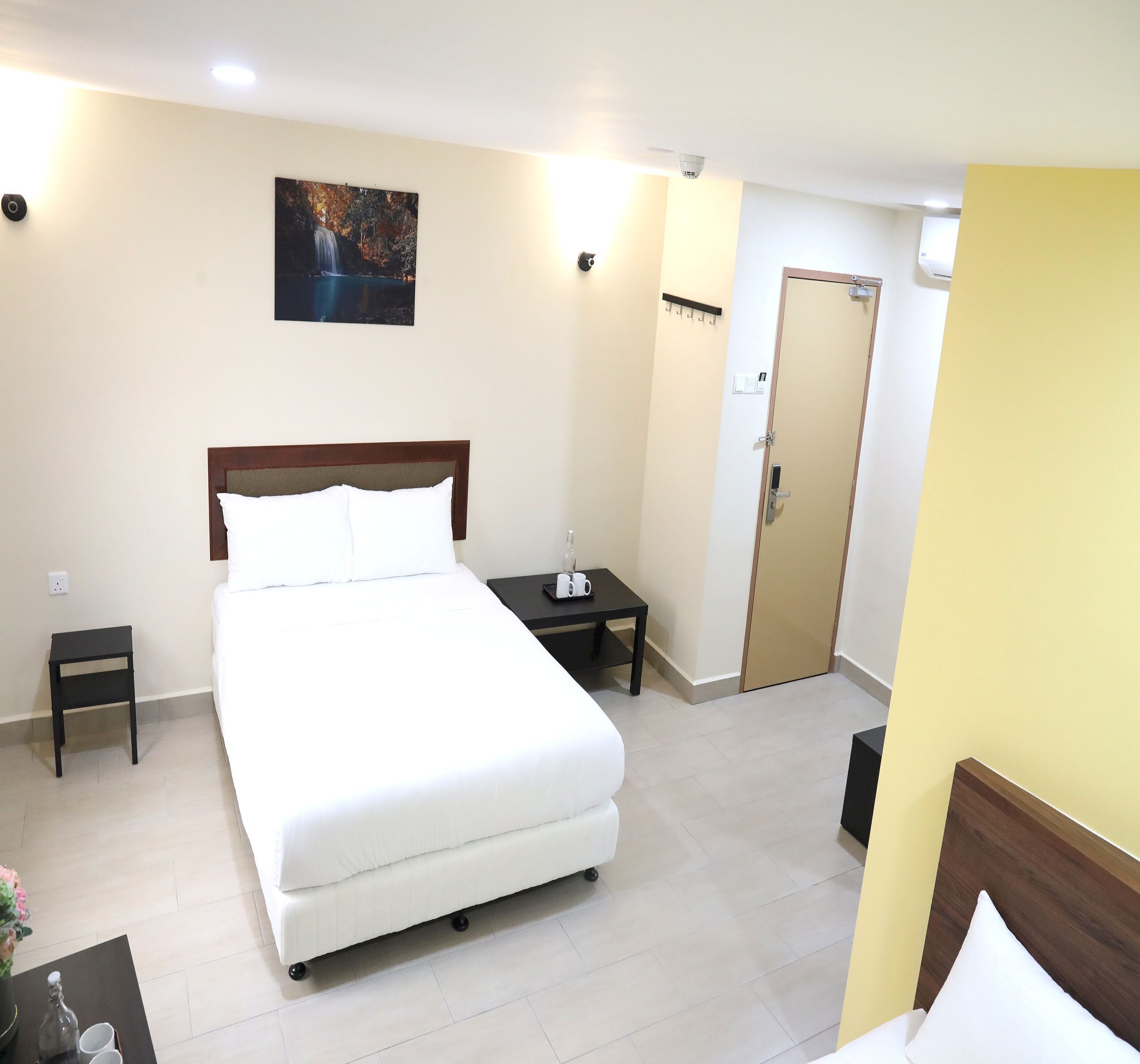 Habitación de hotel ordenada con una cama grande, mesitas de noche, una mesita auxiliar, una obra de arte colgada en la pared y una puerta.