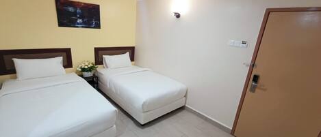 Habitación de hotel con dos camas individuales, una mesita con un jarrón de flores, un cuadro en la pared y una puerta con cerradura.