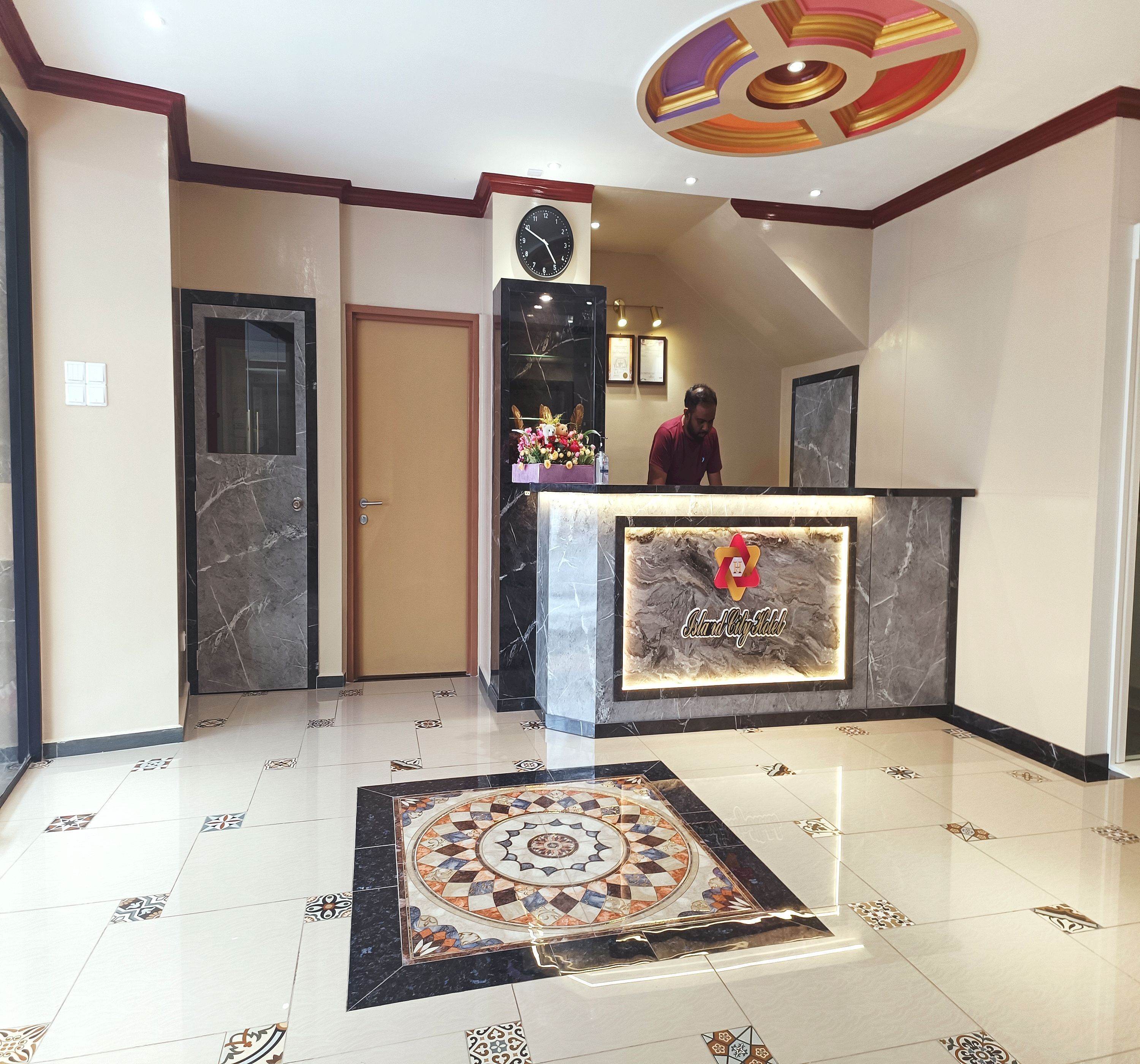 Zona de recepción de un hotel con un mostrador de mármol, un reloj y una alfombra decorativa.