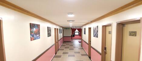 Um corredor de hotel com piso xadrez, portas em ambos os lados e obras de arte nas paredes.