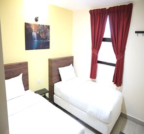 Une chambre d’hôtel avec deux lits, un tableau au mur et une fenêtre avec des rideaux rouges.
