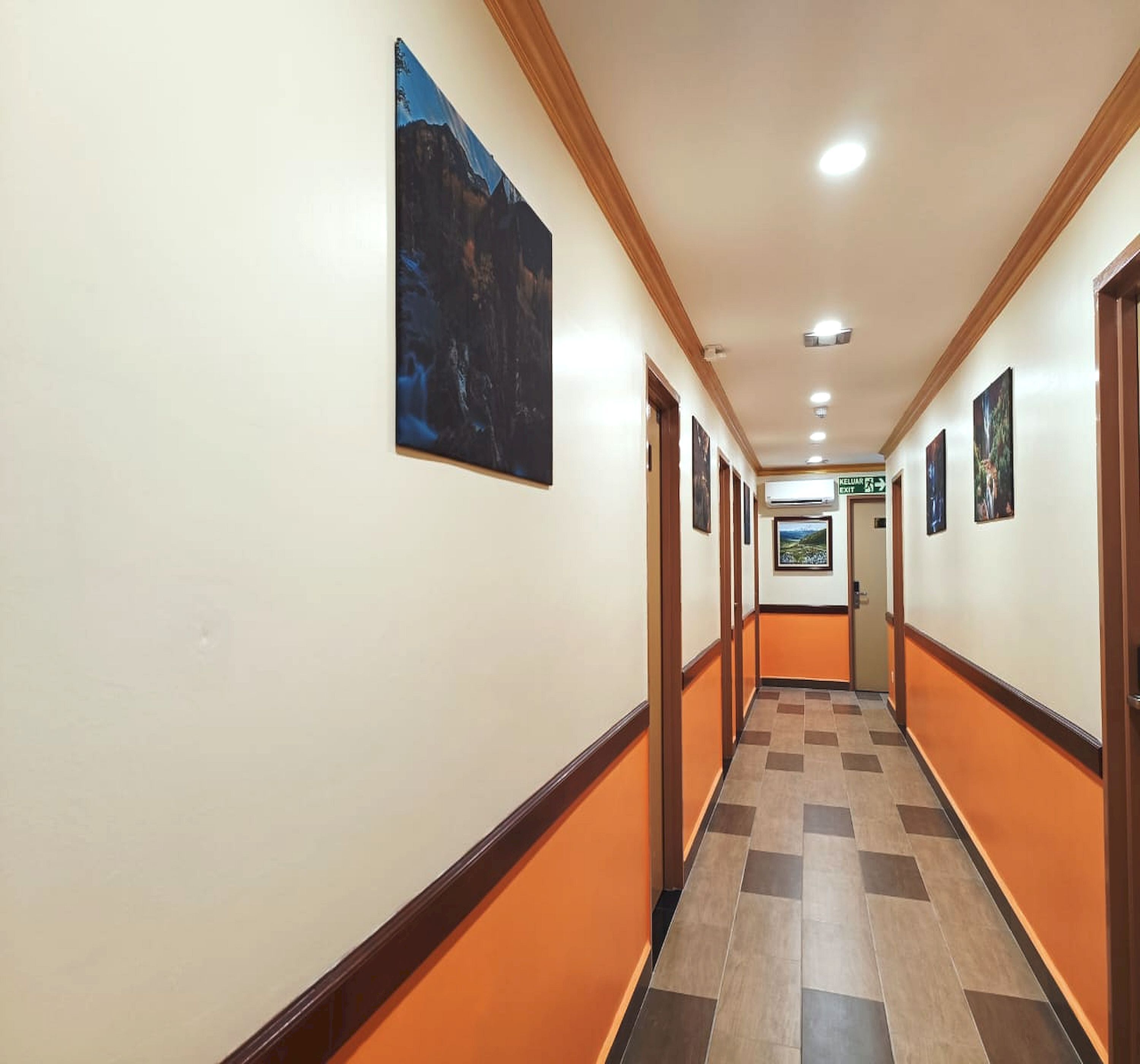 Un pasillo de hotel con piso de diseño a cuadros, obras de arte enmarcadas en las paredes y un letrero que indica la salida.