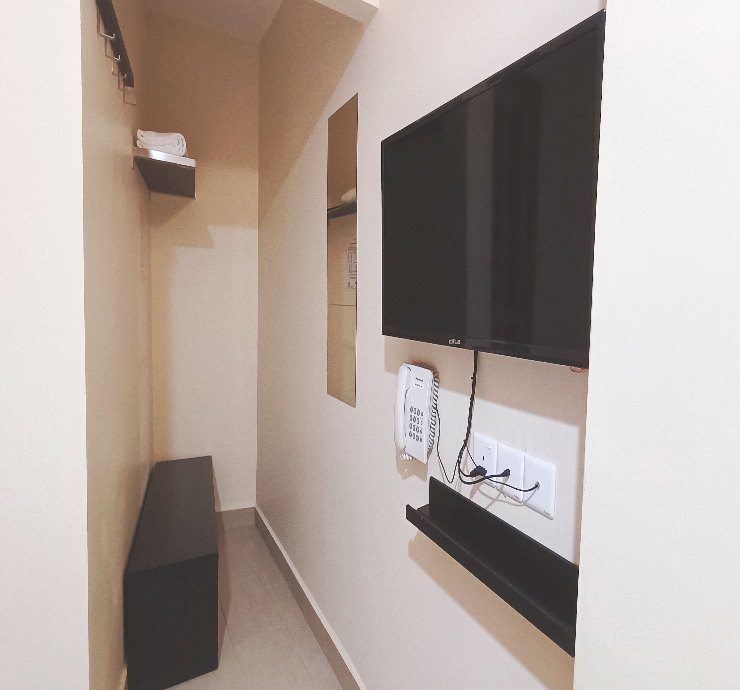 A narrow hallway with a flat-screen TV mounted on the wall, a telephone, and a small shelf with a towel.