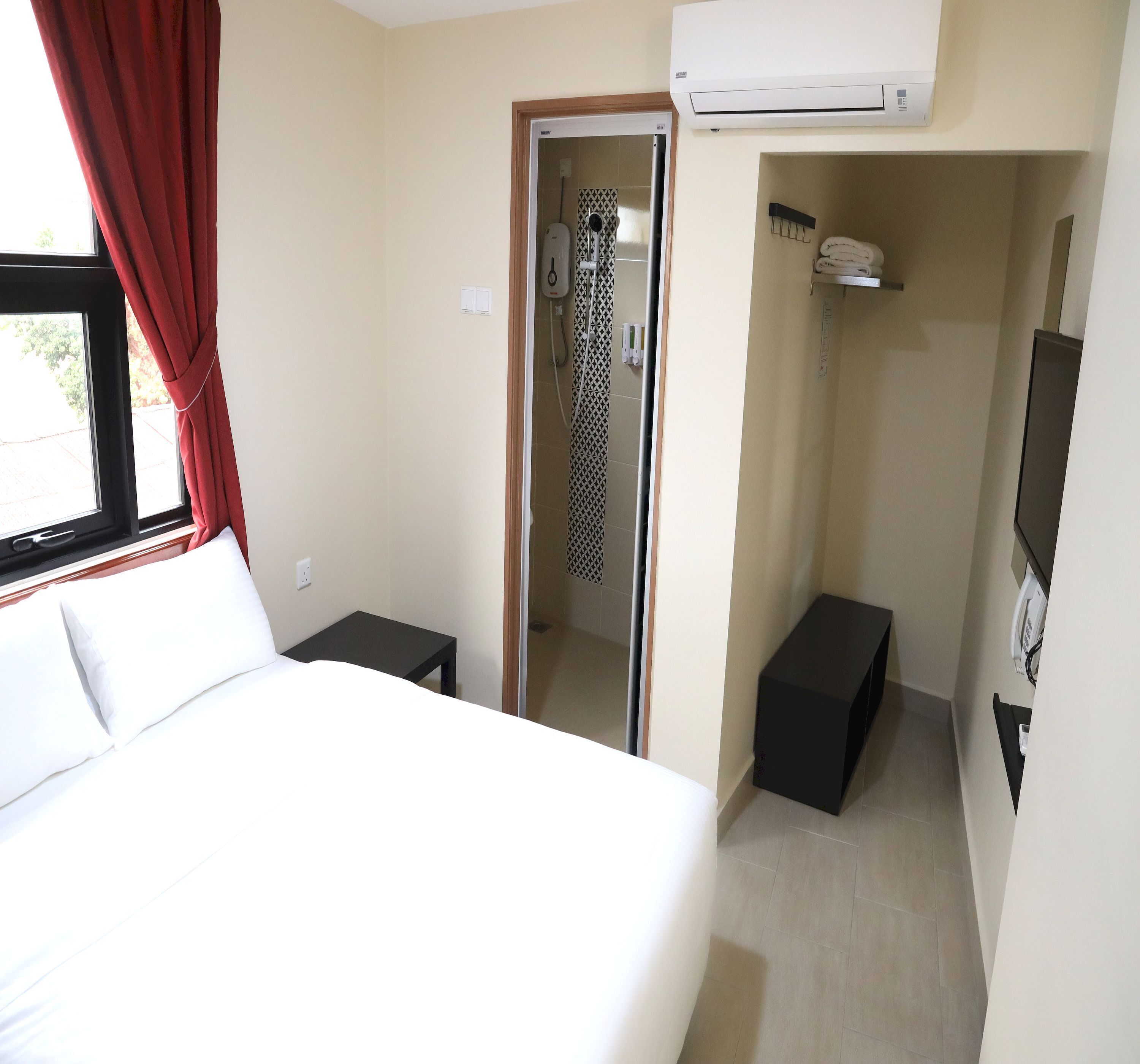 Ein Hotelzimmer mit Bett, kleinem Tisch, Duschbereich und Wand-Fernseher.