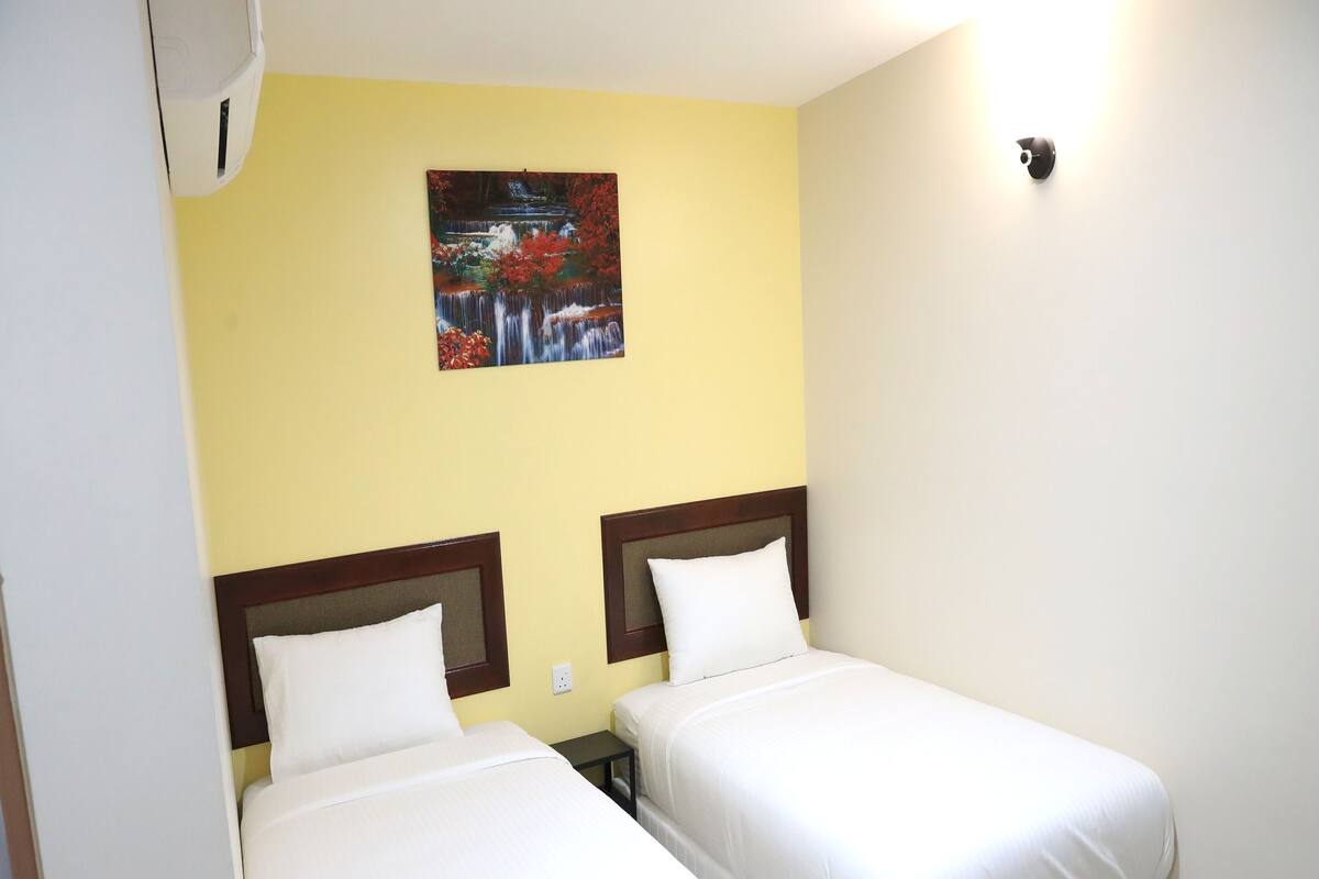 A hotel room with two single beds, a small bedside table, and a wall-mounted light fixture.