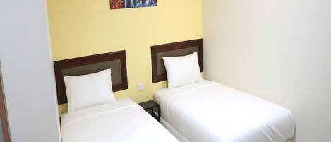Habitación de hotel con dos camas individuales, una mesita de noche pequeña y un aplique de pared.