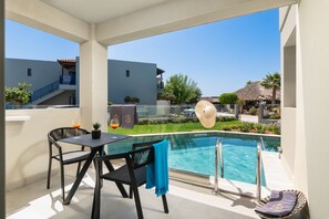 Un balcon avec une piscine, deux chaises, une table et un chapeau posé sur la rambarde.