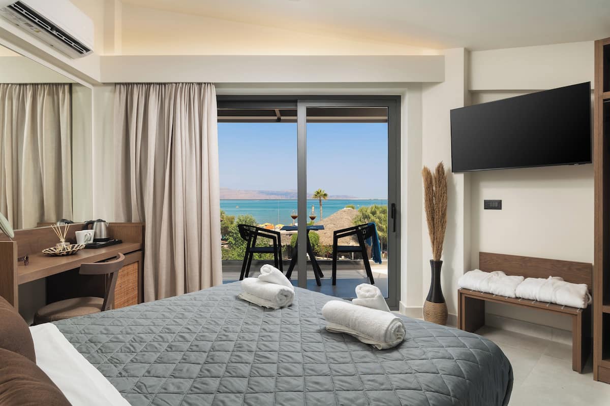 Une chambre d’hôtel comprenant un lit, un bureau, une chaise, une télévision et un balcon avec vue sur la mer.