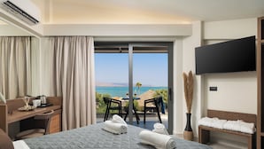 Hotelkamer met een bed, bureau, stoel, televisie en balkon met uitzicht op zee.