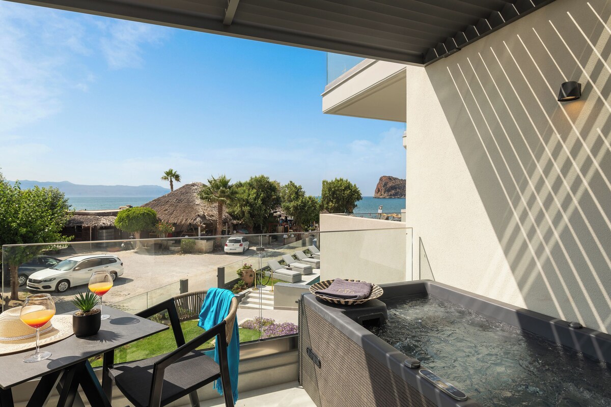 Een balkon met een jacuzzi, een tafel met drankjes en uitzicht op zee en bergen.
