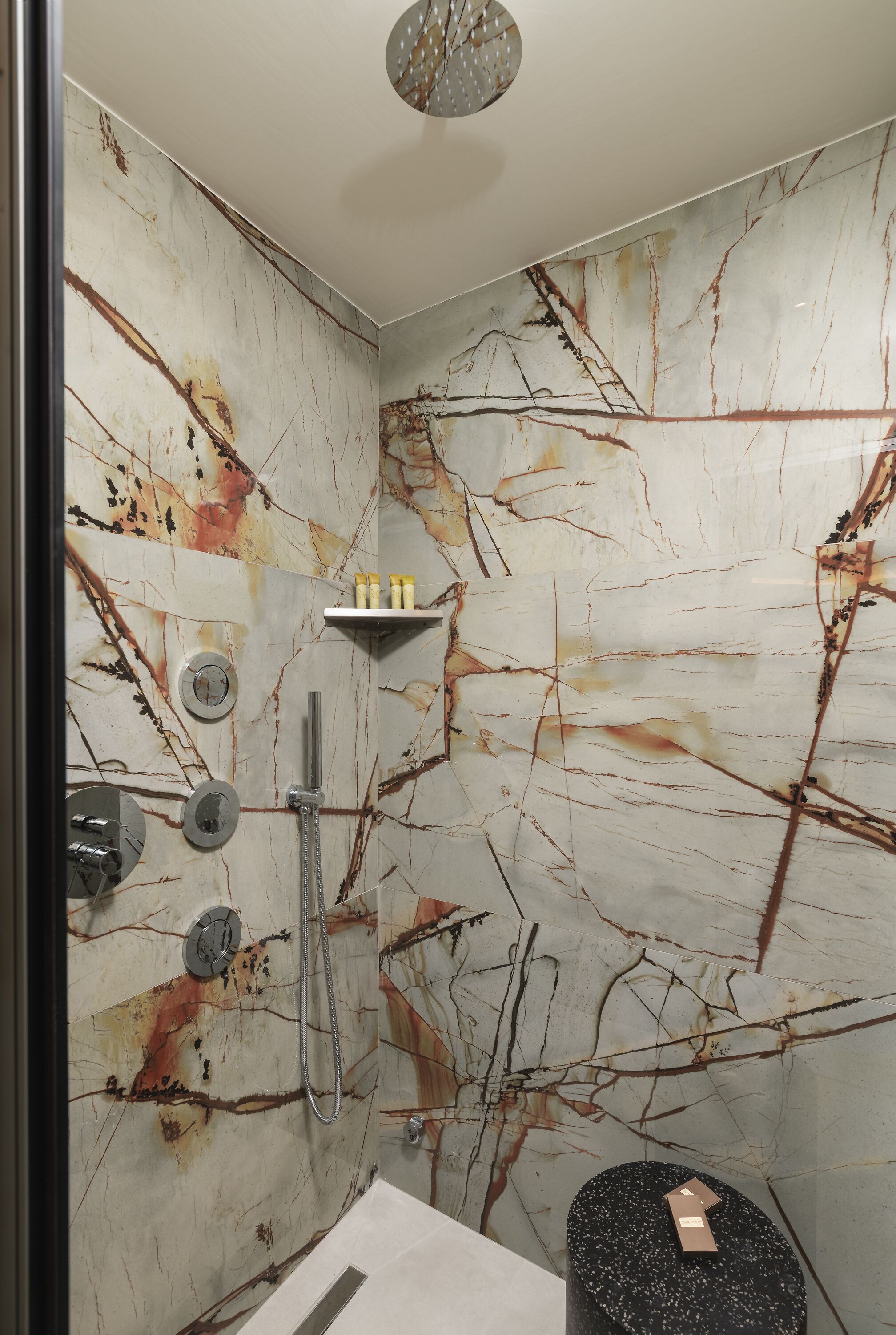 A bathroom with a marble wall, a shower, and a toilet.