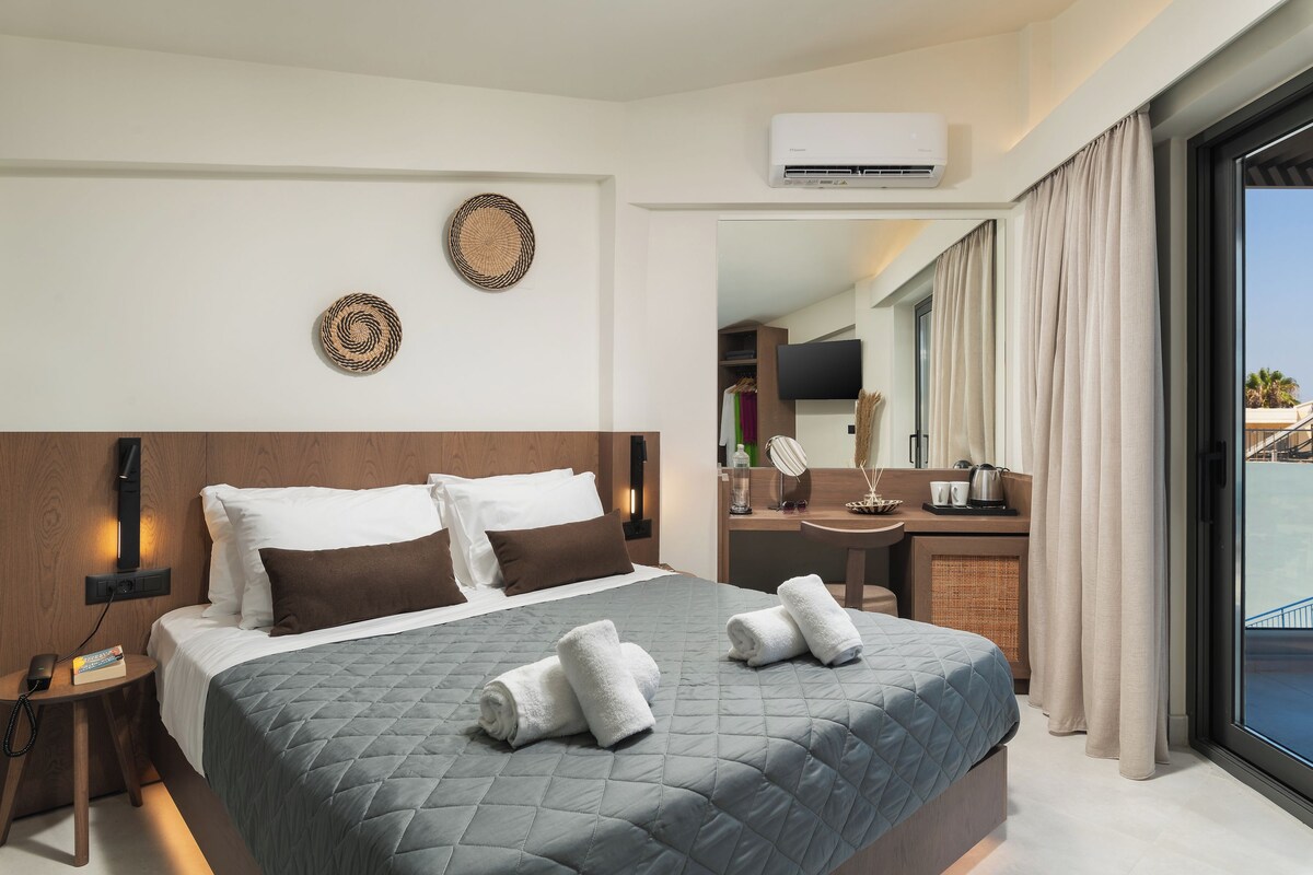 Een moderne hotelkamer met een groot bed, een nachtkastje met een lamp, een flatscreen-tv en uitzicht op het zwembad door het raam.