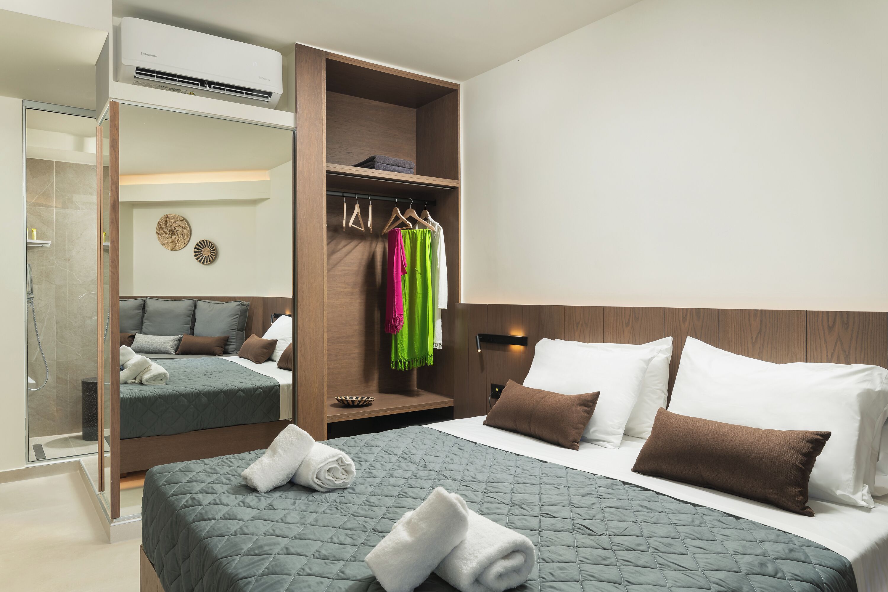 A hotel room with a bed, a wardrobe, a mirror, and a shower.